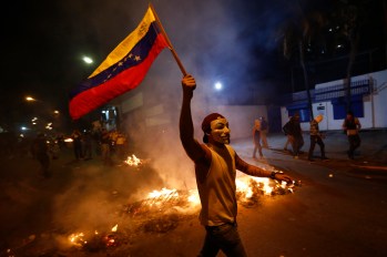 An opposition demonstrators holds a Venezuelan flag in front of a burning barricade during a protest against President Nicolas Maduro's government in Caracas February 15, 2014. Protesters gathered to demand the president's resignation, denouncing him over grievances ranging from political repression to daily issues such as inflation, shortages of basic products, and rampant crime.